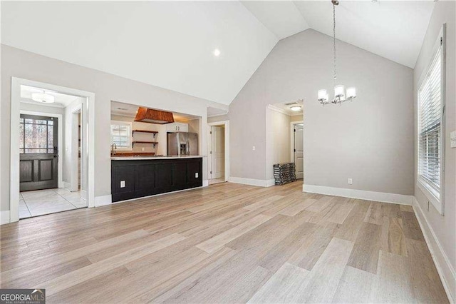 unfurnished living room with baseboards, high vaulted ceiling, a chandelier, and light wood finished floors