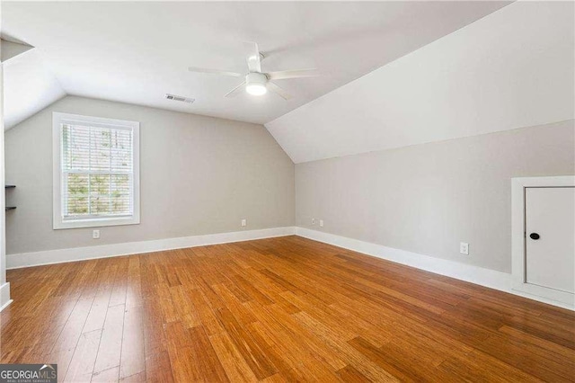 additional living space with a ceiling fan, visible vents, baseboards, vaulted ceiling, and wood-type flooring