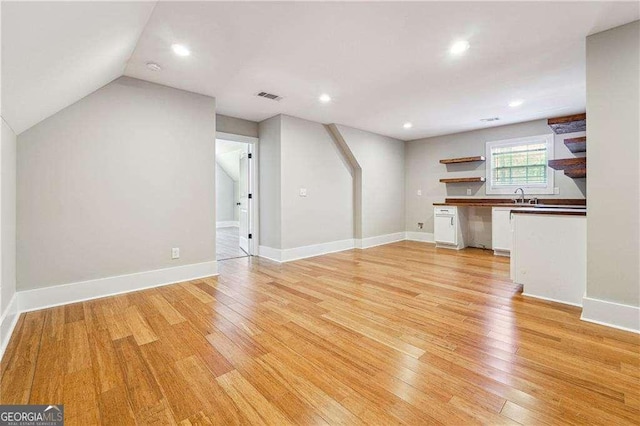 unfurnished living room with visible vents, lofted ceiling, recessed lighting, light wood finished floors, and baseboards