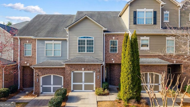 townhome / multi-family property featuring brick siding, an attached garage, concrete driveway, and a shingled roof