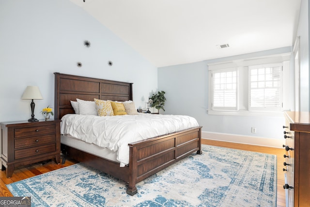 bedroom featuring visible vents, baseboards, wood finished floors, and vaulted ceiling