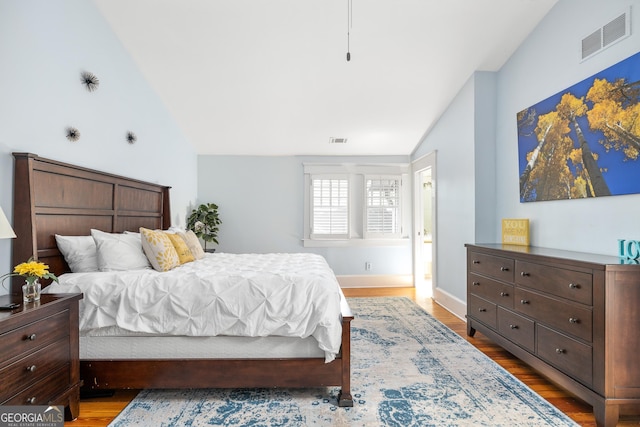 bedroom featuring visible vents, baseboards, wood finished floors, and vaulted ceiling