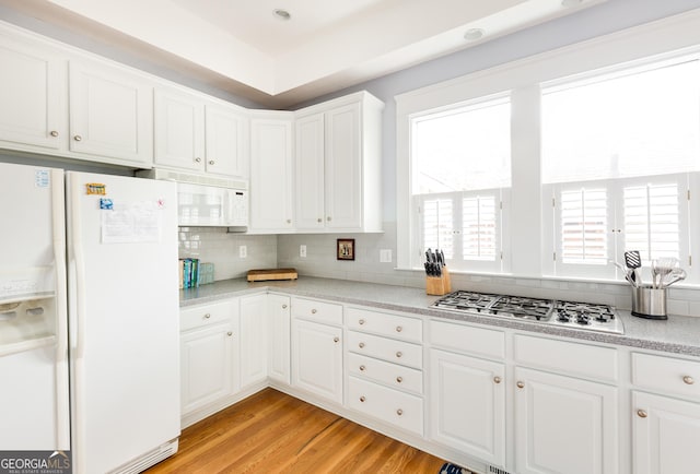 kitchen featuring light wood-type flooring, tasteful backsplash, white cabinetry, white appliances, and light countertops