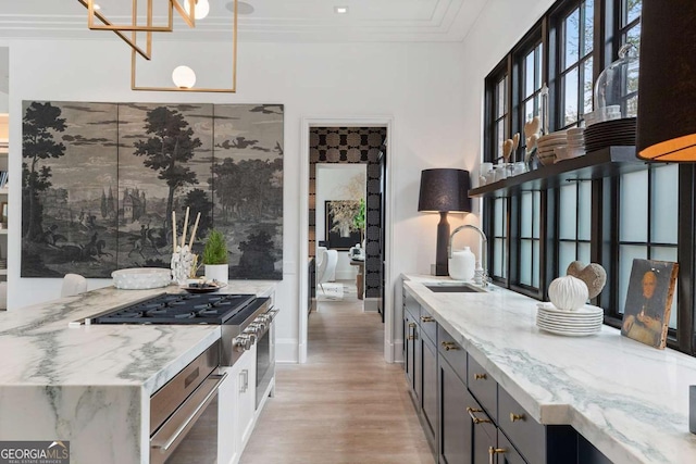 kitchen featuring crown molding, light wood-type flooring, light stone counters, appliances with stainless steel finishes, and a sink