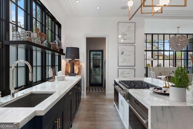 kitchen featuring a sink, ornamental molding, light stone counters, a notable chandelier, and dark cabinets