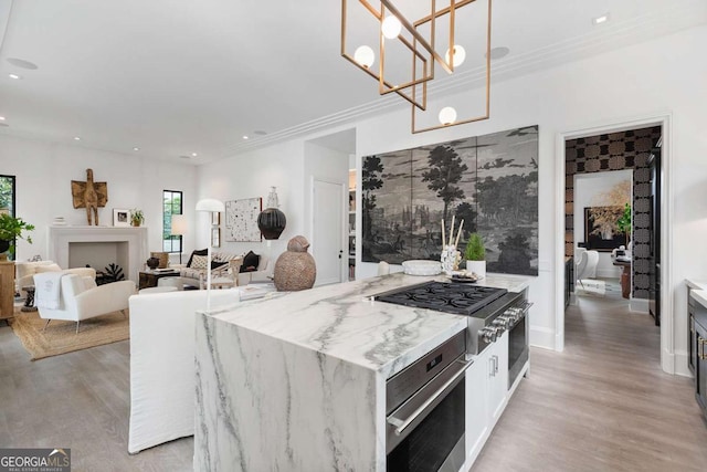 kitchen with light stone counters, light wood-style floors, crown molding, stainless steel oven, and cooktop