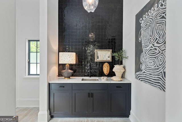 bar featuring a sink, backsplash, bar, light wood finished floors, and baseboards