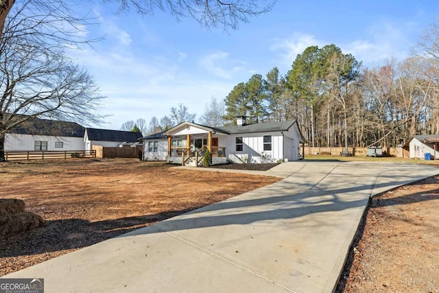 view of front of home with an attached garage, board and batten siding, fence, a porch, and driveway