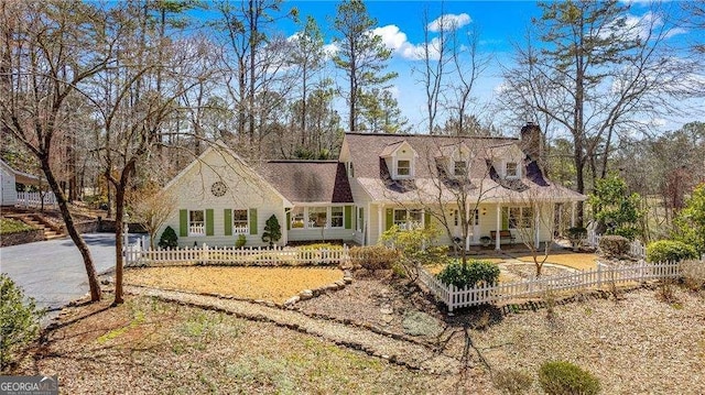 cape cod house with aphalt driveway, a fenced front yard, and a chimney