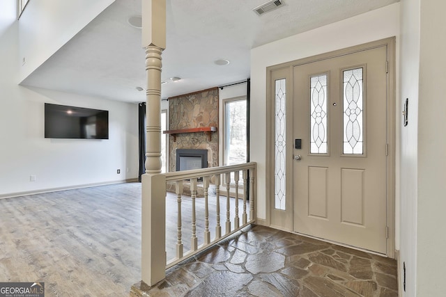 entryway featuring stone finish floor, a fireplace, visible vents, and baseboards