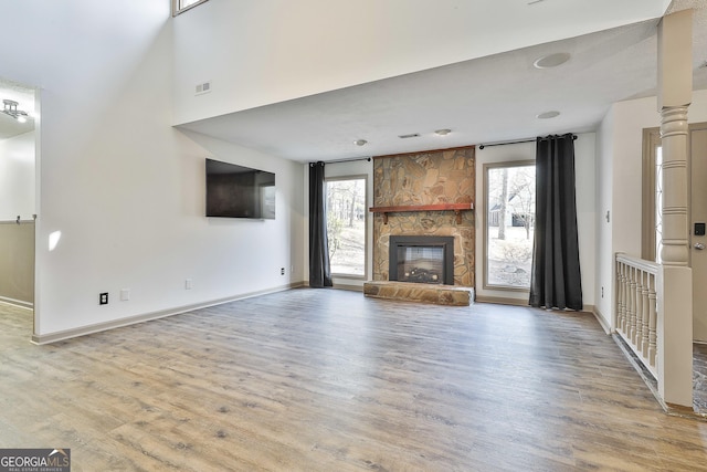 unfurnished living room featuring a stone fireplace, wood finished floors, a healthy amount of sunlight, and baseboards