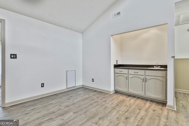 unfurnished room with visible vents, baseboards, lofted ceiling, light wood-style floors, and a sink