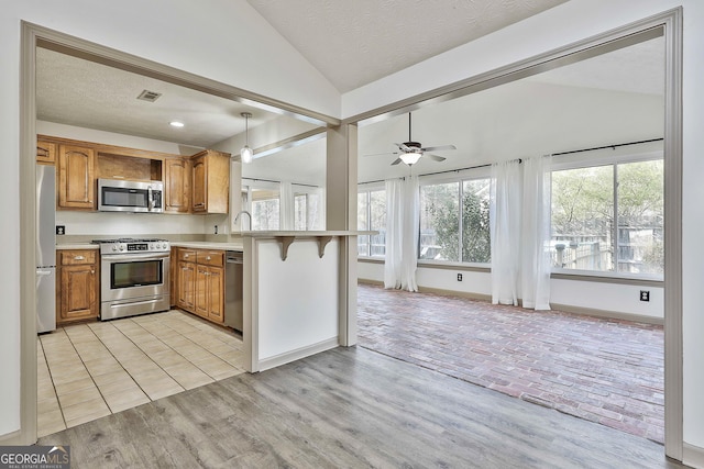 kitchen featuring brown cabinetry, stainless steel appliances, vaulted ceiling, light countertops, and light wood-style floors