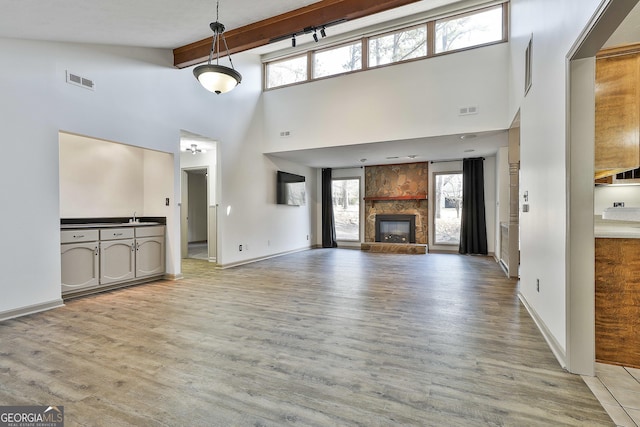 unfurnished living room with beam ceiling, visible vents, a stone fireplace, and light wood-style floors