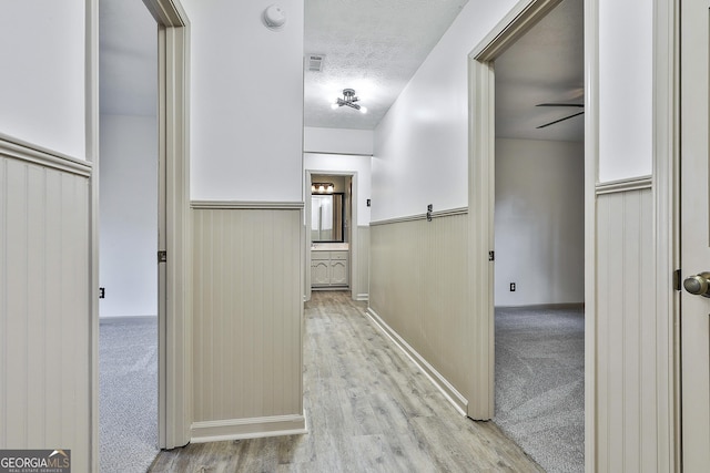 corridor featuring carpet, wood finished floors, a wainscoted wall, and a textured ceiling