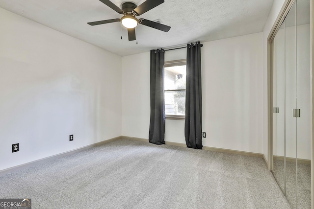 unfurnished bedroom featuring light carpet, a ceiling fan, a textured ceiling, a closet, and baseboards