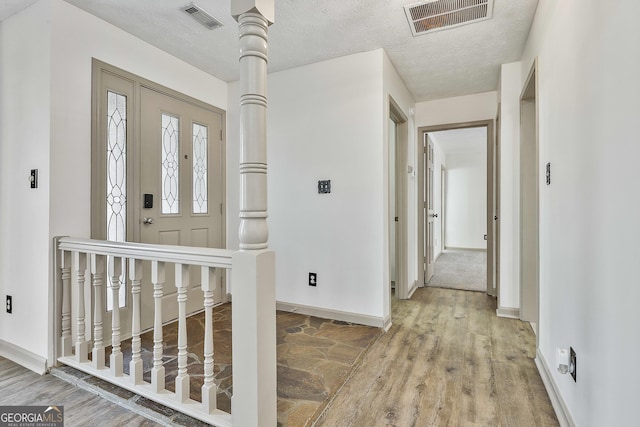 foyer entrance featuring visible vents, baseboards, a textured ceiling, and light wood-style flooring