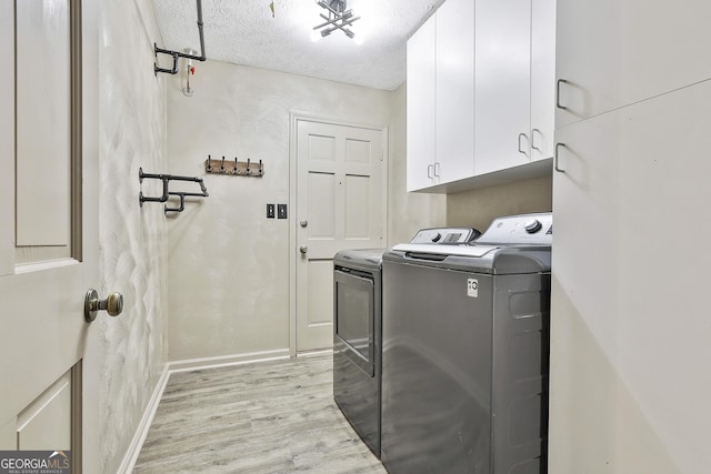 laundry area with baseboards, light wood-style floors, cabinet space, a textured ceiling, and separate washer and dryer