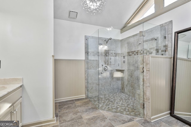 full bathroom featuring a wainscoted wall, stone finish flooring, an inviting chandelier, a shower stall, and vanity