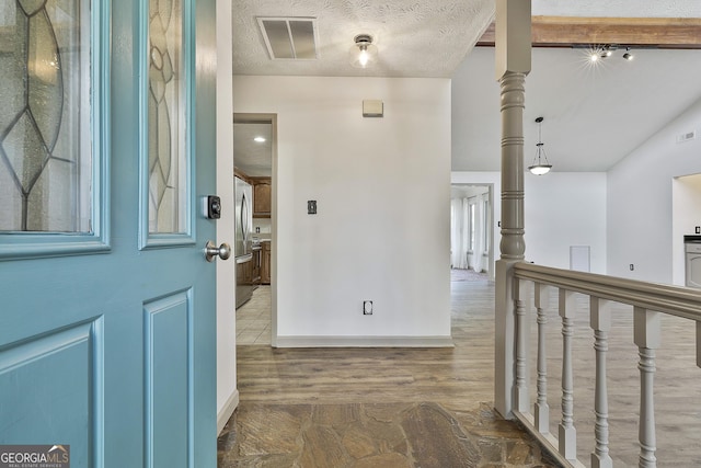 foyer entrance featuring baseboards, wood finished floors, visible vents, and a textured ceiling