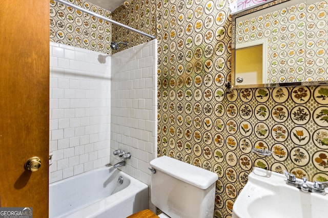 bathroom featuring wallpapered walls, toilet, bathtub / shower combination, and a sink