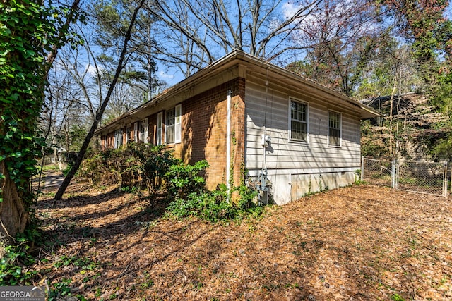 view of side of property featuring crawl space, fence, brick siding, and a gate