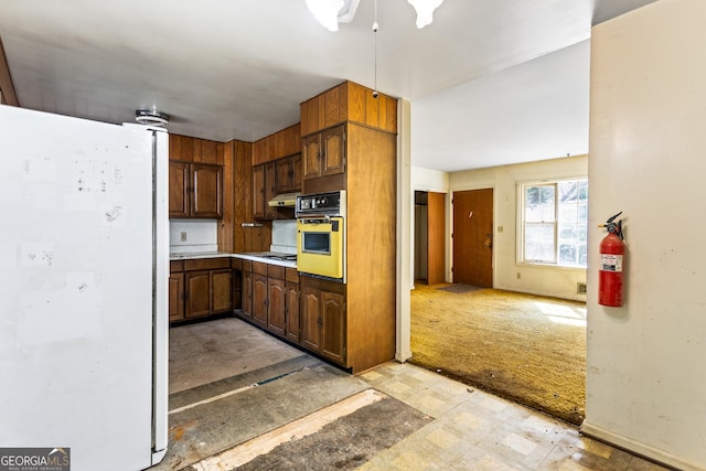 kitchen featuring oven, under cabinet range hood, light floors, freestanding refrigerator, and gas cooktop