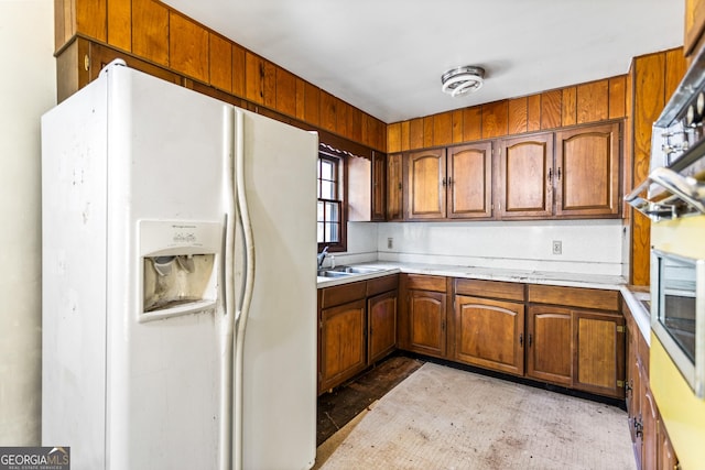 kitchen featuring brown cabinetry, a sink, light countertops, and white fridge with ice dispenser