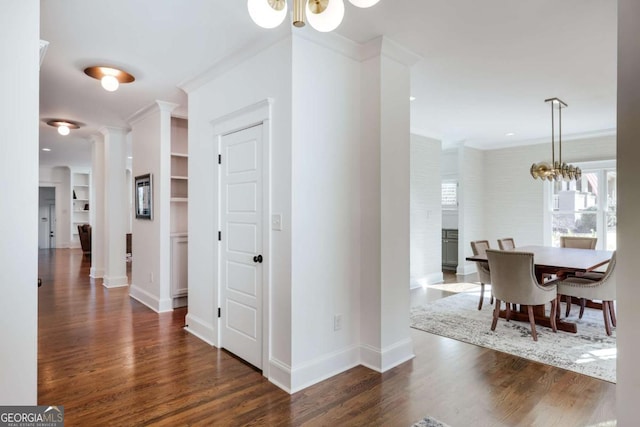 hall with baseboards, ornamental molding, wood finished floors, a notable chandelier, and ornate columns