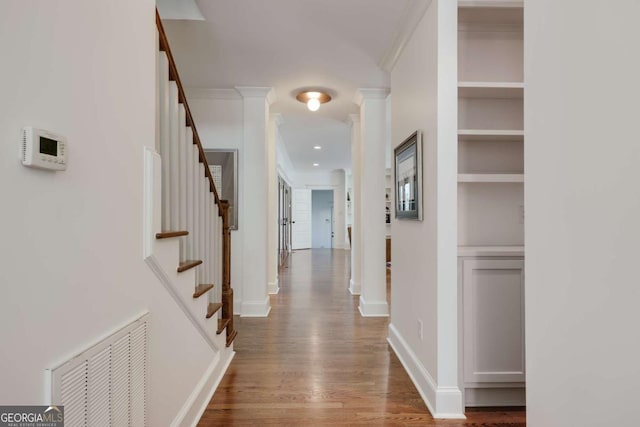 corridor with stairway, wood finished floors, visible vents, decorative columns, and crown molding