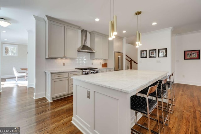 kitchen with a kitchen island, a breakfast bar, appliances with stainless steel finishes, wall chimney exhaust hood, and dark wood-style flooring