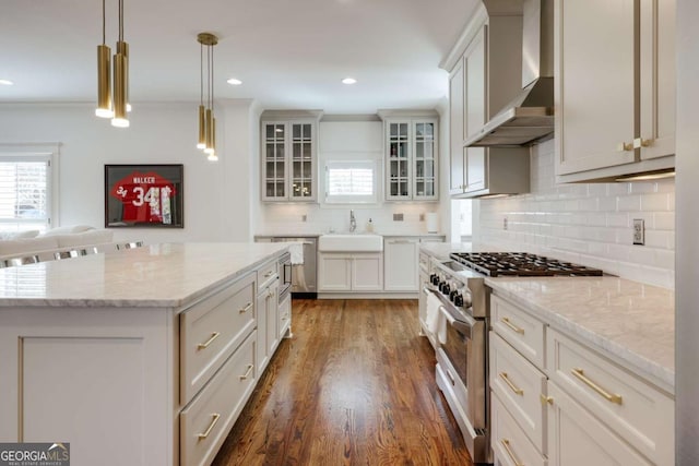 kitchen with dark wood-style floors, a sink, high end stove, wall chimney range hood, and backsplash