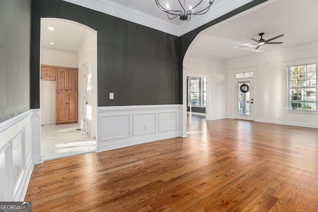 unfurnished living room featuring a healthy amount of sunlight, arched walkways, and ornamental molding