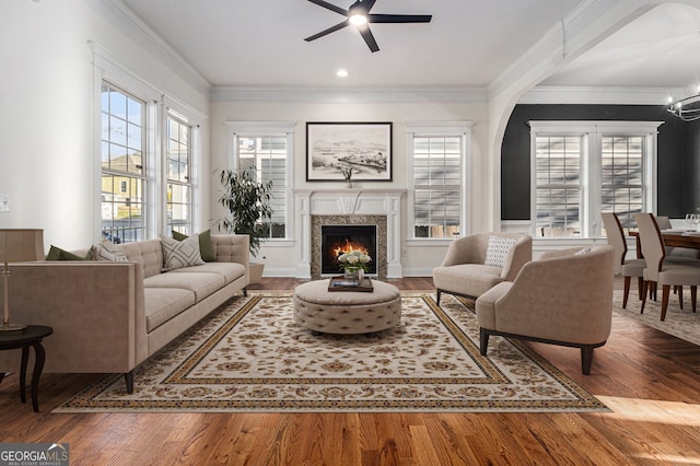 living area with a premium fireplace, wood finished floors, ceiling fan, and ornamental molding