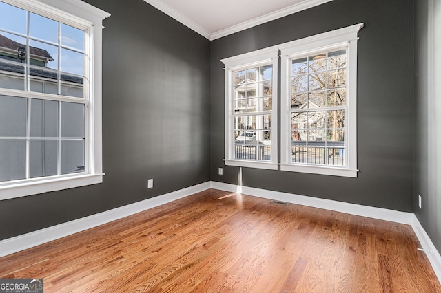 unfurnished room with crown molding, wood finished floors, baseboards, and visible vents