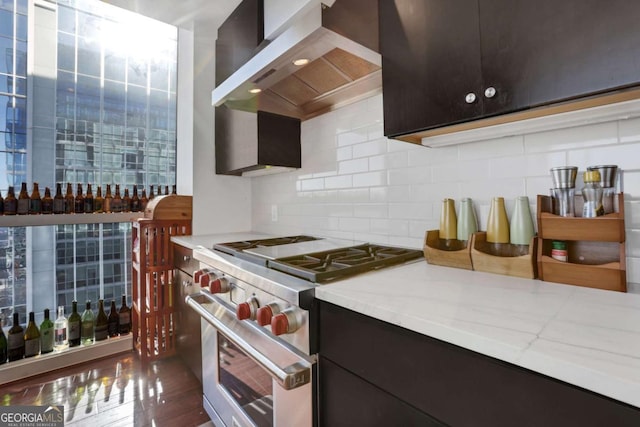 kitchen with backsplash, high end stainless steel range, dark brown cabinetry, light stone counters, and wall chimney exhaust hood