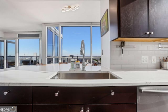 kitchen with a sink, dark brown cabinets, light stone countertops, decorative backsplash, and stainless steel dishwasher