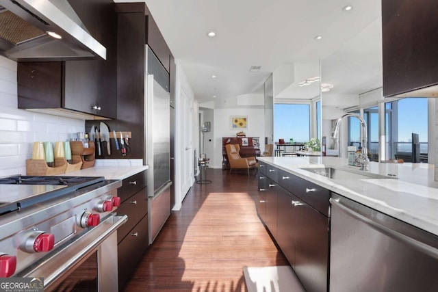 kitchen with dark wood-type flooring, a sink, backsplash, appliances with stainless steel finishes, and wall chimney range hood