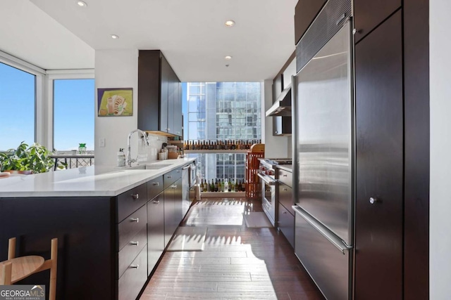 kitchen with dark wood-style flooring, a sink, light countertops, wall chimney exhaust hood, and premium appliances