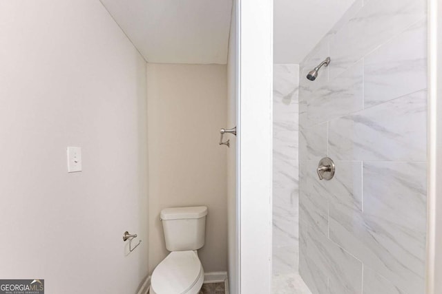 bathroom featuring toilet, baseboards, and tiled shower