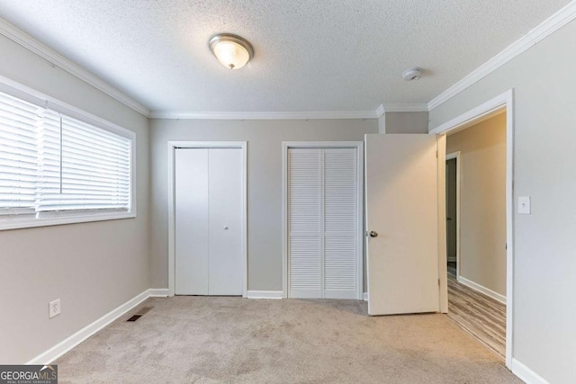 unfurnished bedroom with baseboards, visible vents, carpet floors, ornamental molding, and two closets