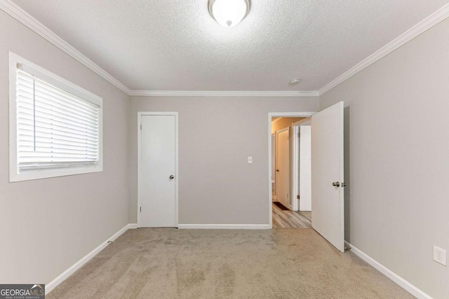 unfurnished bedroom with light colored carpet, a textured ceiling, baseboards, and ornamental molding