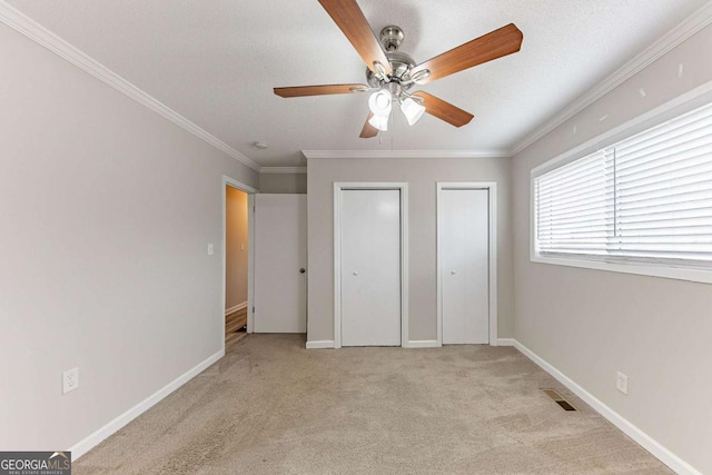 unfurnished bedroom with visible vents, crown molding, baseboards, multiple closets, and light carpet