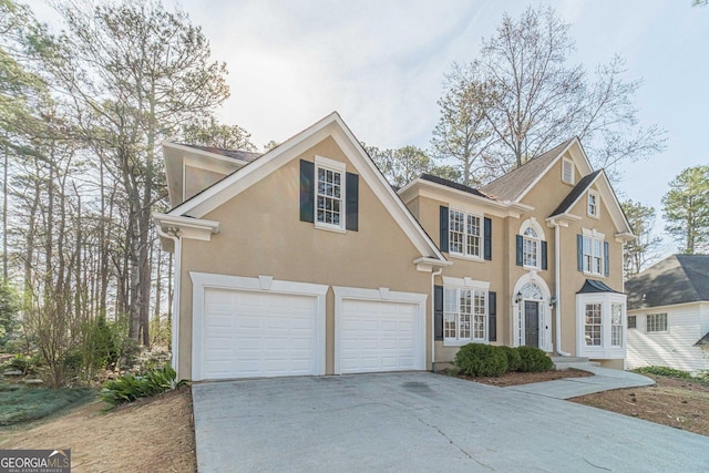 colonial house with stucco siding, an attached garage, and driveway