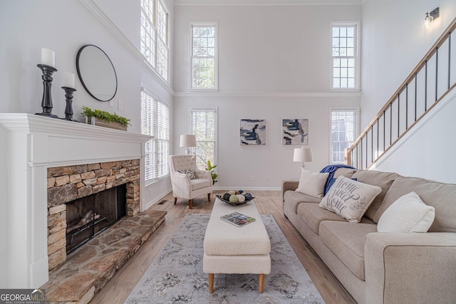 living room featuring baseboards, light wood-style floors, a stone fireplace, and a healthy amount of sunlight