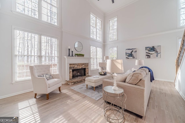 living room with wood finished floors, a high ceiling, a stone fireplace, crown molding, and baseboards