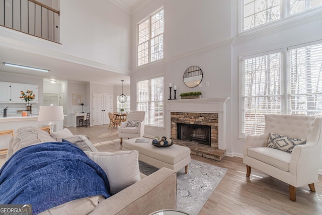 living room featuring a fireplace, crown molding, a healthy amount of sunlight, and light wood-type flooring