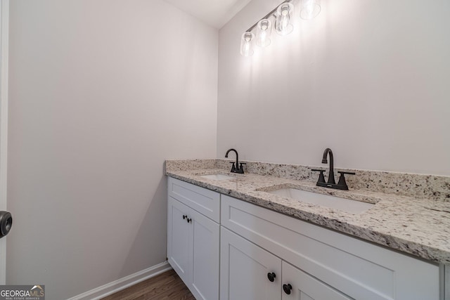 bathroom with double vanity, wood finished floors, baseboards, and a sink