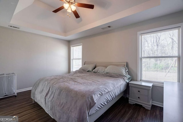 bedroom with a raised ceiling, dark wood-style floors, and visible vents