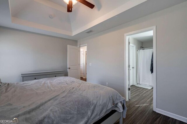 bedroom with baseboards, visible vents, a tray ceiling, dark wood-style flooring, and ceiling fan